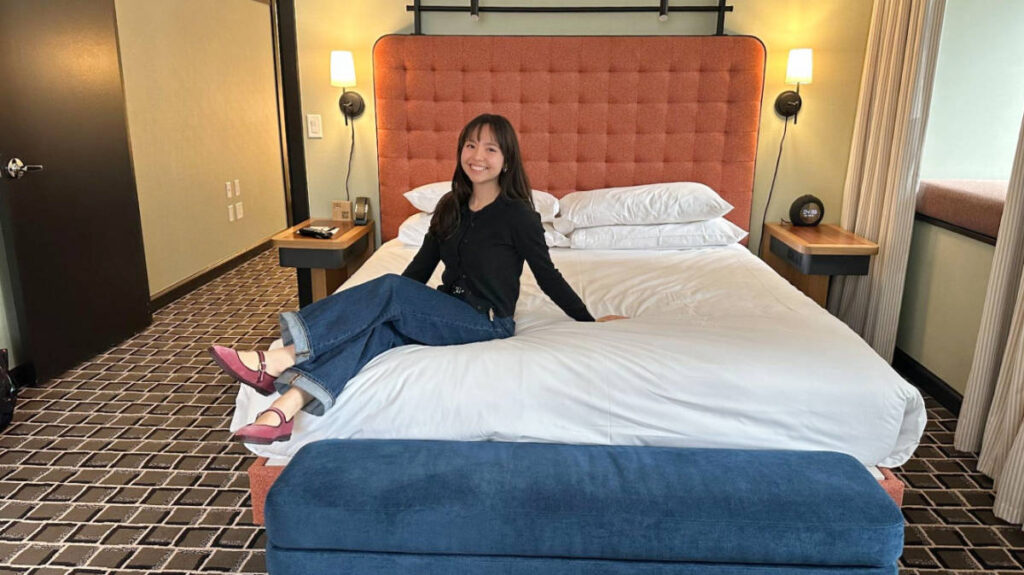 The author, Lea Rose Allbaugh sitting on her bed in L7 Chicago by Lotte