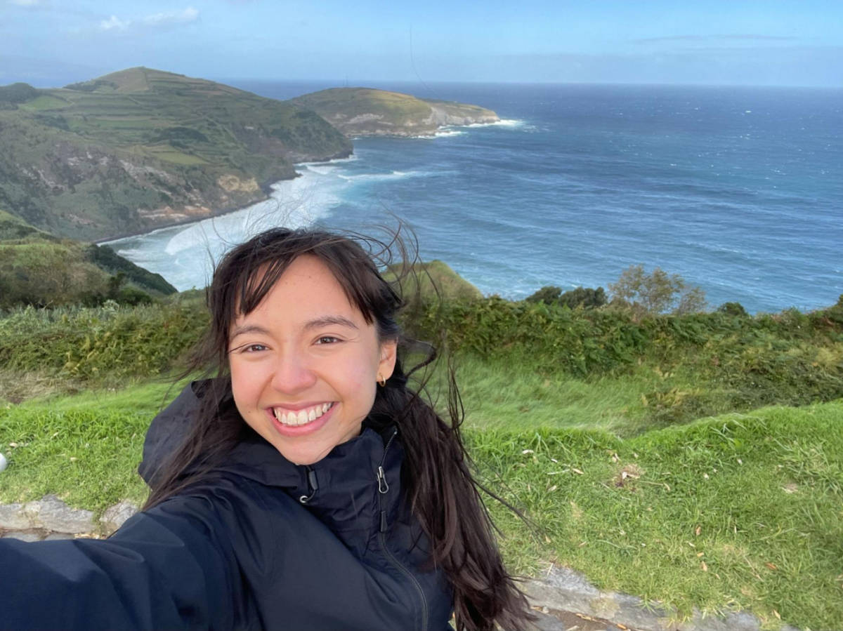 The author Lea Rose Allbaugh, smiling for a photo with São Miguel Island view on a windy day