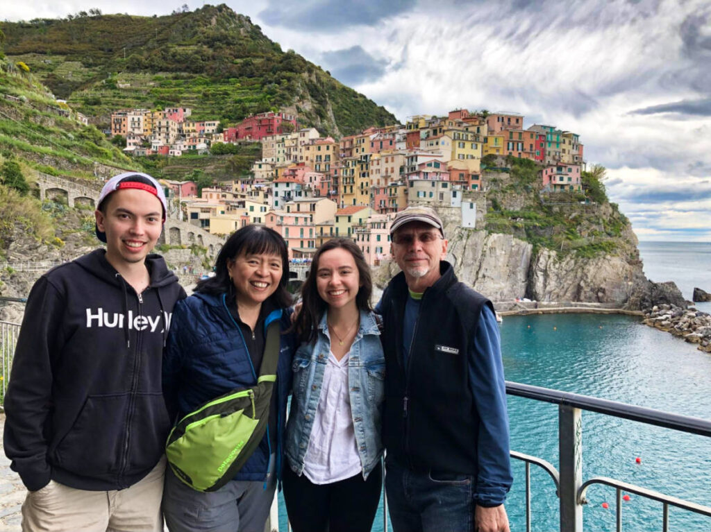 The author Lea Rose and her family taking a photo with the colorful cliffside village in in Manarola