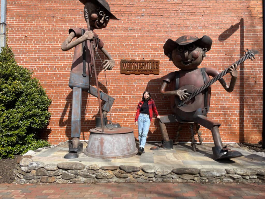 The author, Lea Rose posing for a photo with the sculptures in downtown Waynesville