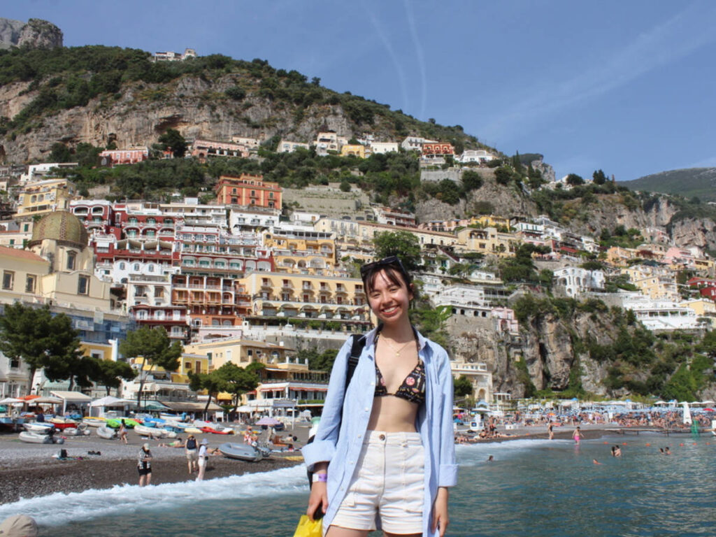 The author Lea Rose Allbaugh, posing for a photo with the colorful Positano village in the background