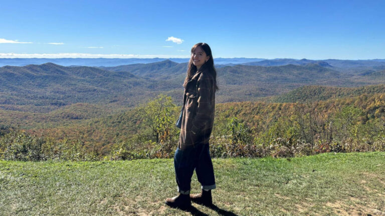 The author Lea Rose Allbaugh, smiling for a photo with the scenic view of the rolling hills in Western North Carolina