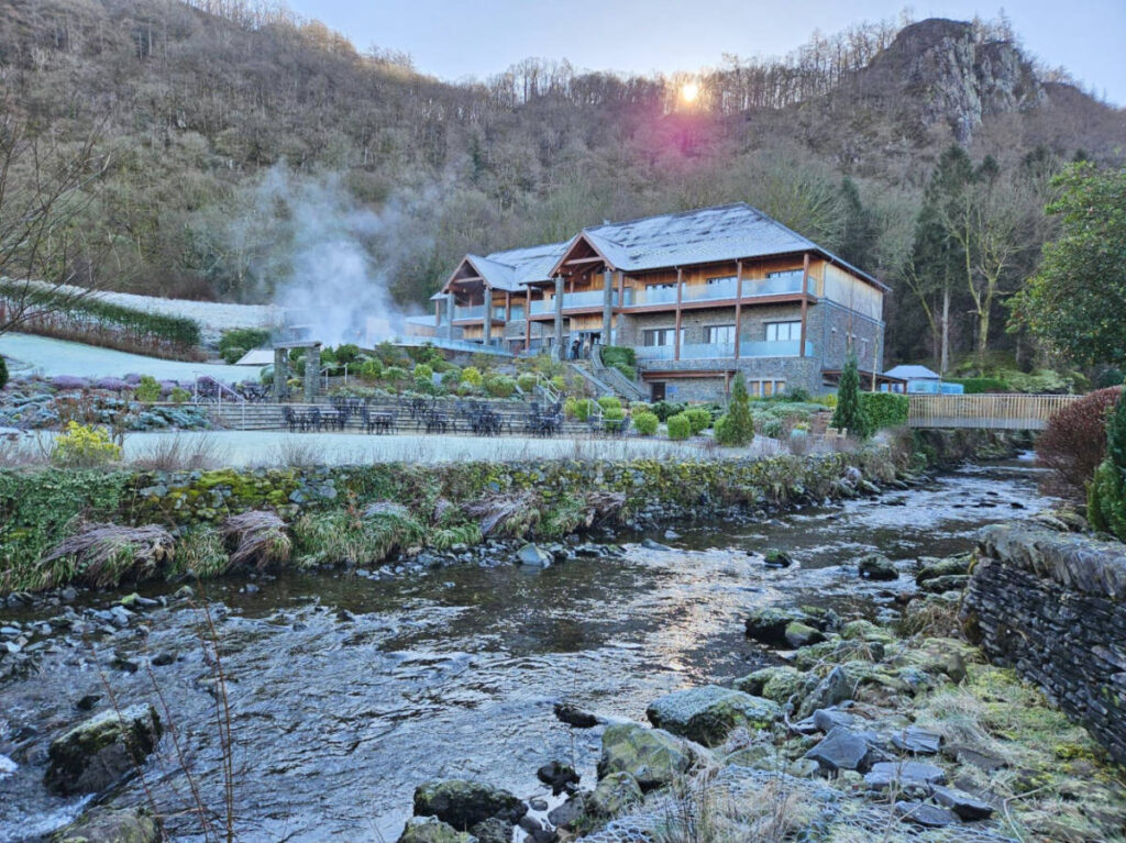 The exterior of Lodore Falls Hotel & Spa surrounded by greenery and a river