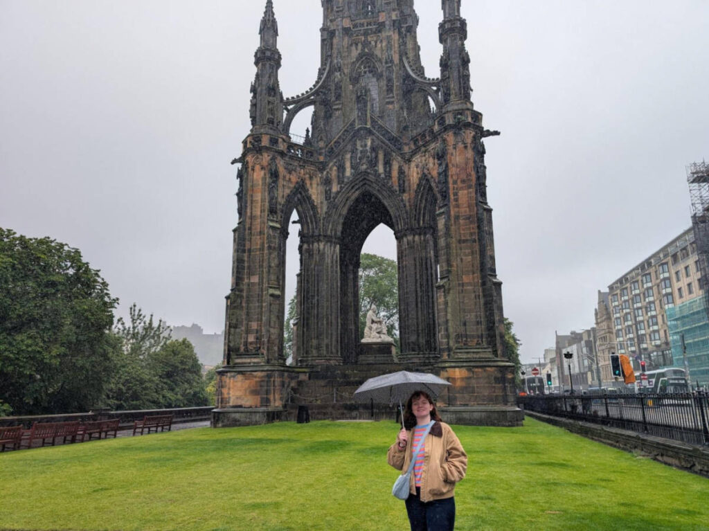 The author Louise Wylie smiling for a photo in front of The Scott Monument Towers