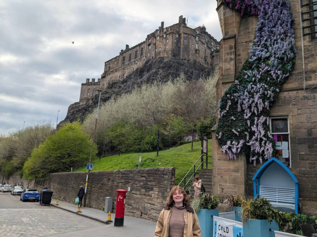 The author Louise Wylie, smiling for a photo with the Edinburgh Castle Towers in the background