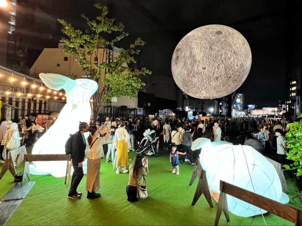 People taking a picture of the moon during the Moon Art Night celebrating the Lunar Festival at Shimokitazawa