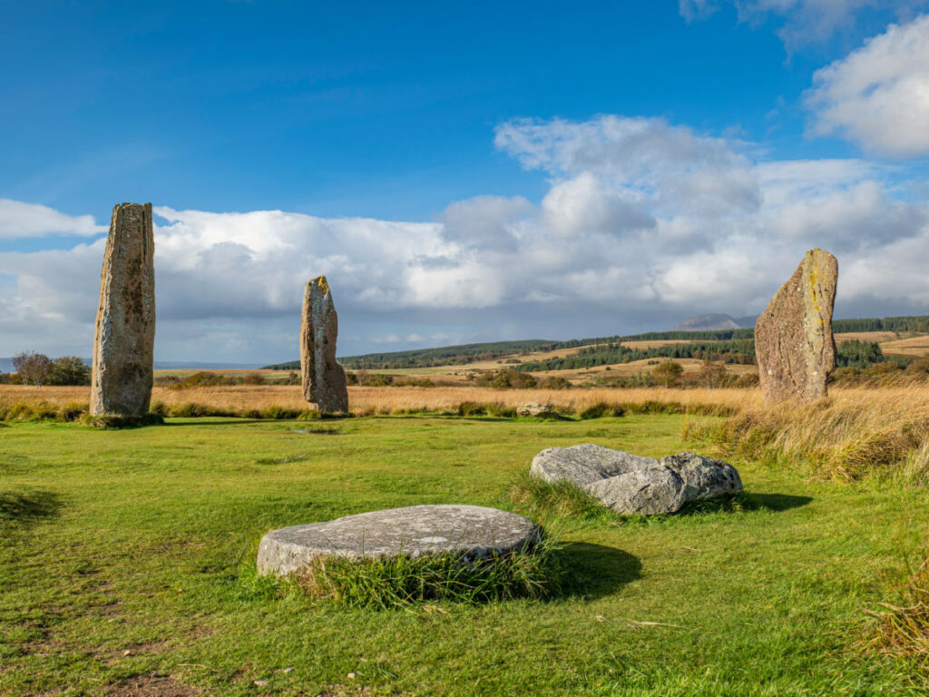 Ancient standing stones of the Machrie Moor Stone Circles rise from a grassy field on the Isle of Arran