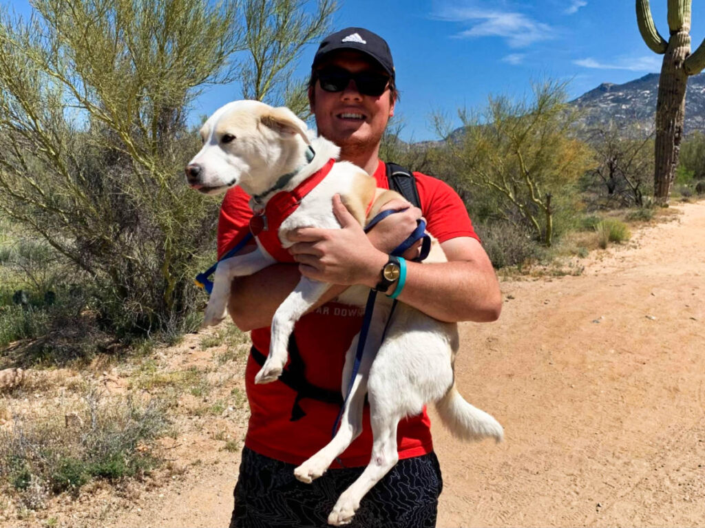 A man carrying the dog on the trail hike