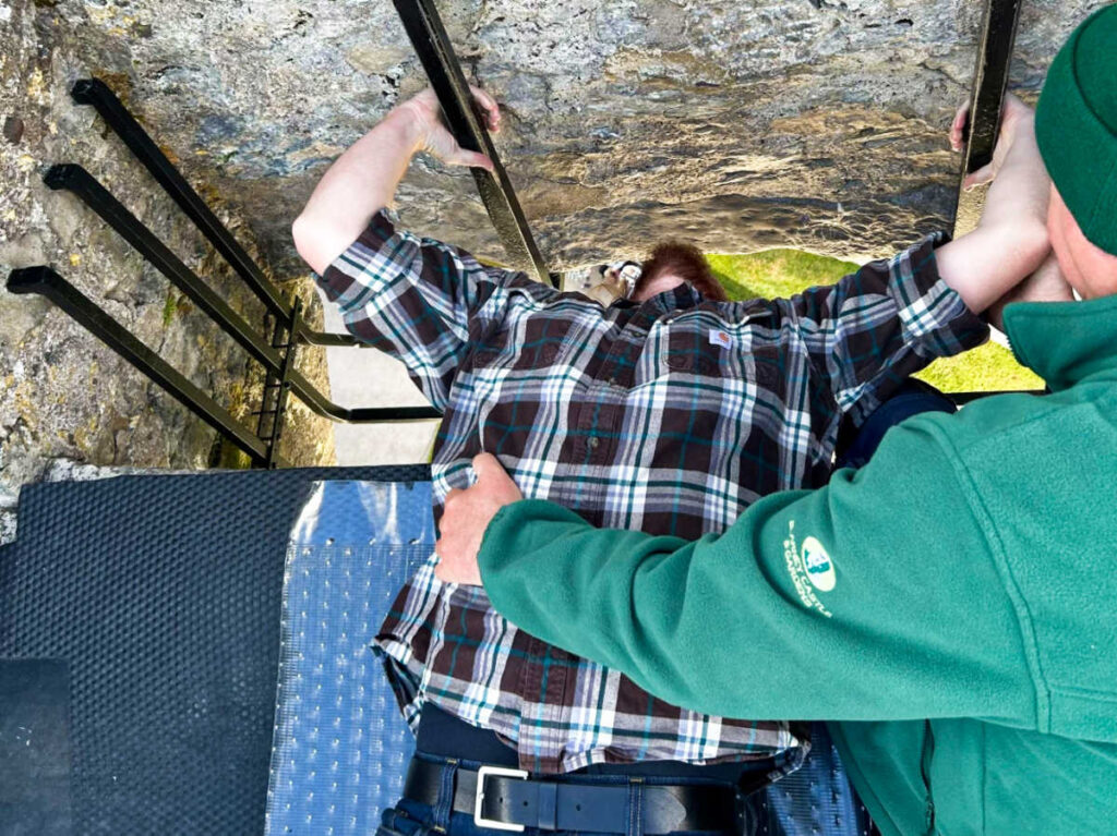 A man helping the  author's husband kissing the Blarney Stone