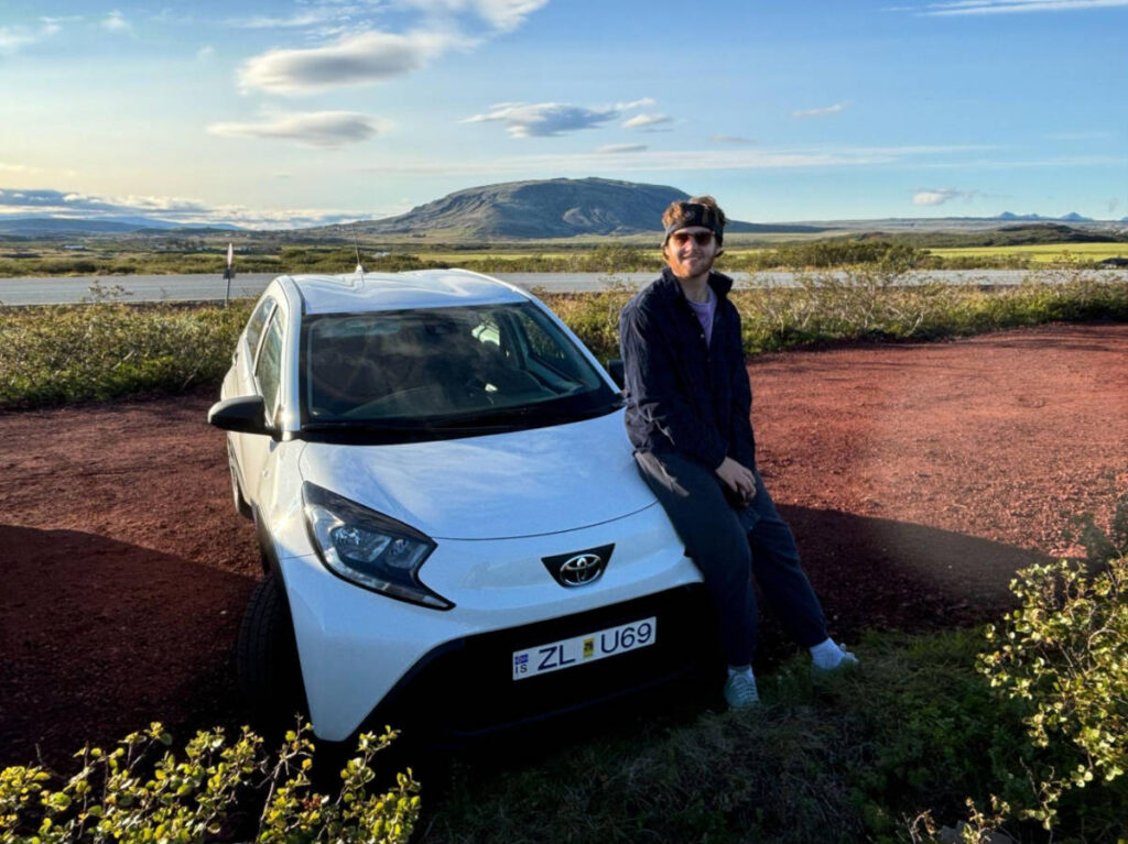 A man sitting on the rented car with a scenic view near the Kerid Crater on the Golden Circle