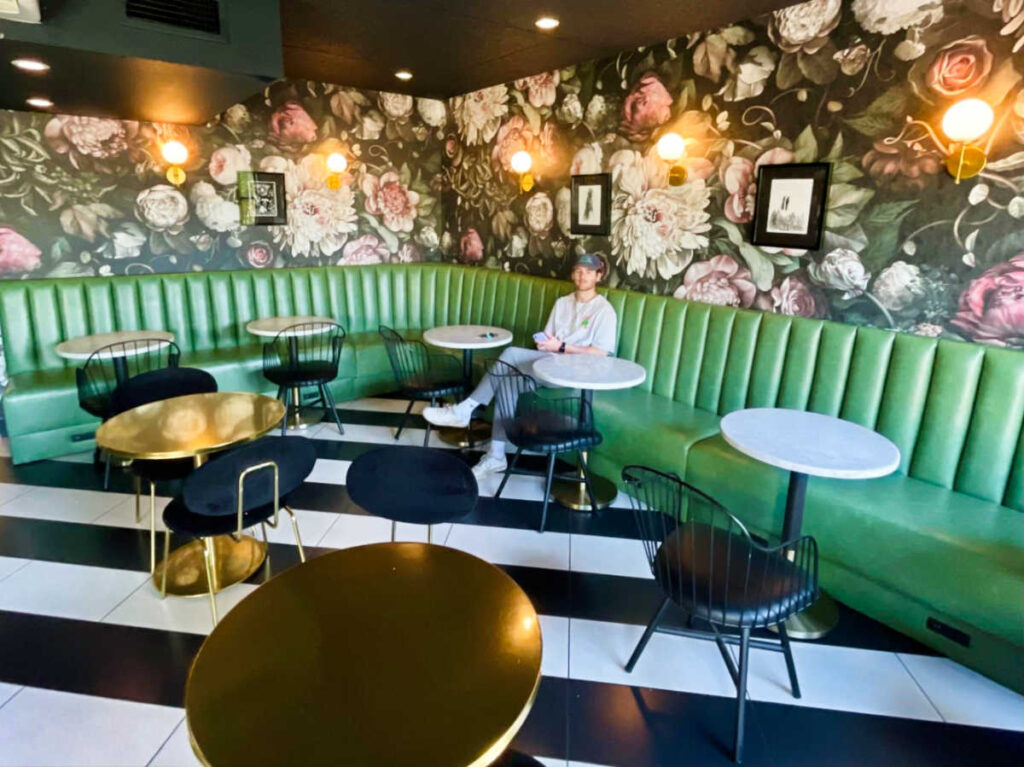 A man sitting in the middle of the floral and green interior of Dark Hall Coffee