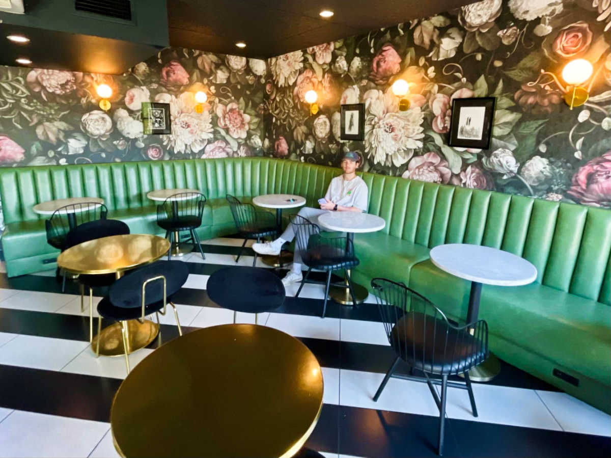 A man sitting in the middle of the floral and green interior of Dark Hall Coffee
