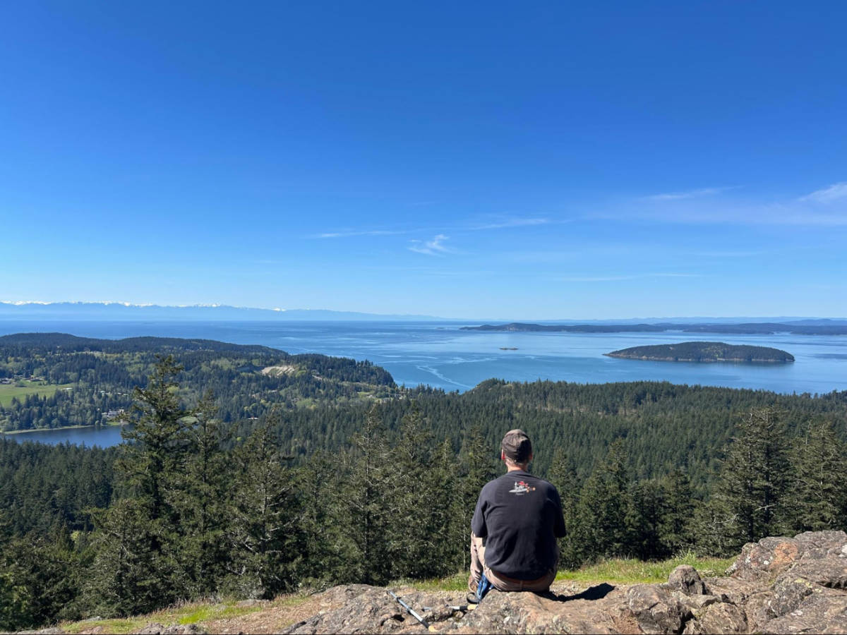 A man sitting on the rock admiring the overlooking view from Sugarloaf Mountain on Fidalgo Island