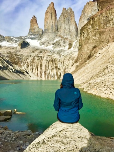 The author McKenna Mobley, sitting on a rock while admiring the view of Torres del Paine Towers