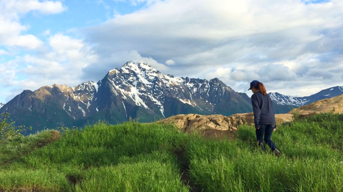 Travel Lemming Writer, McKenna walking along the grass landscape with mountain view in the background