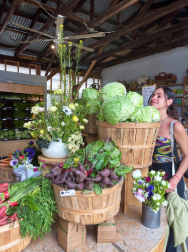 The author McKenna Mobley, posing for a photo near the baskets of fresh vegetables at The Ecology Center