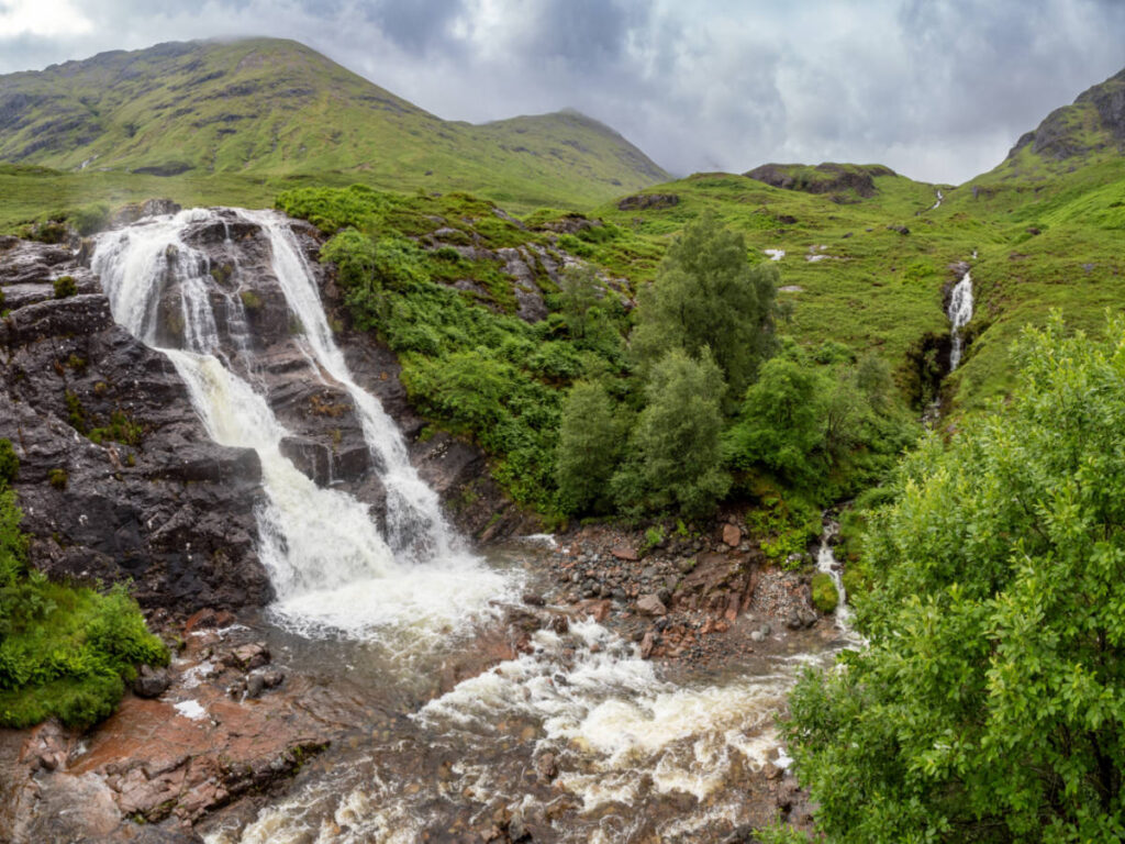 Meeting of Three Waters cascades down surrounded by lush green hills