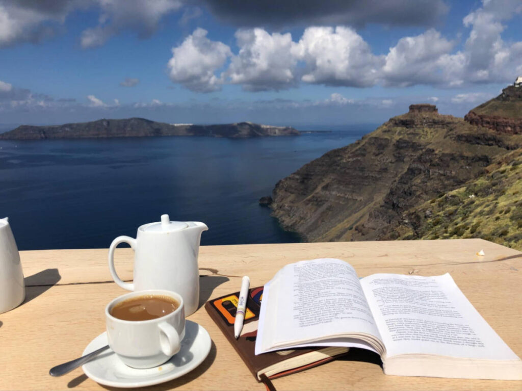 A cup of coffee and a book on the table with an overlooking views of the islands in Santorini