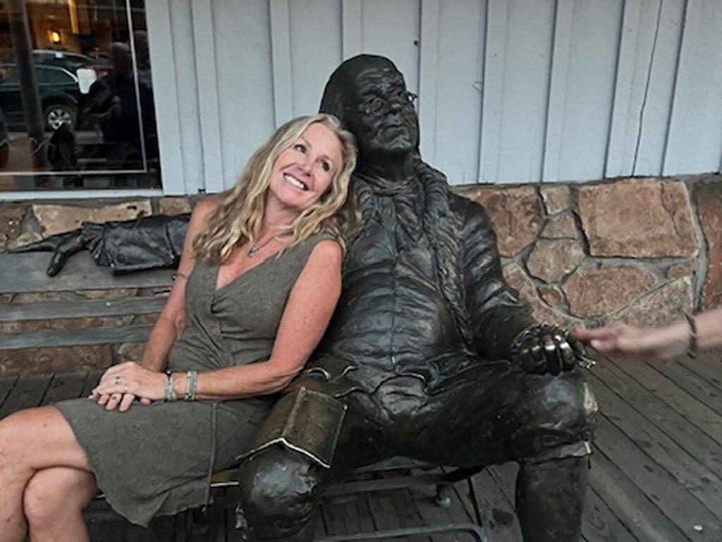 The author Morri Stewart posing for a photo with the statue of Ben Franklin on the bench