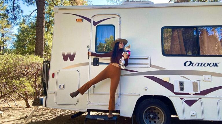 The author McKenna Mobley with her dog posing on the ladder of her motorhome at a campground