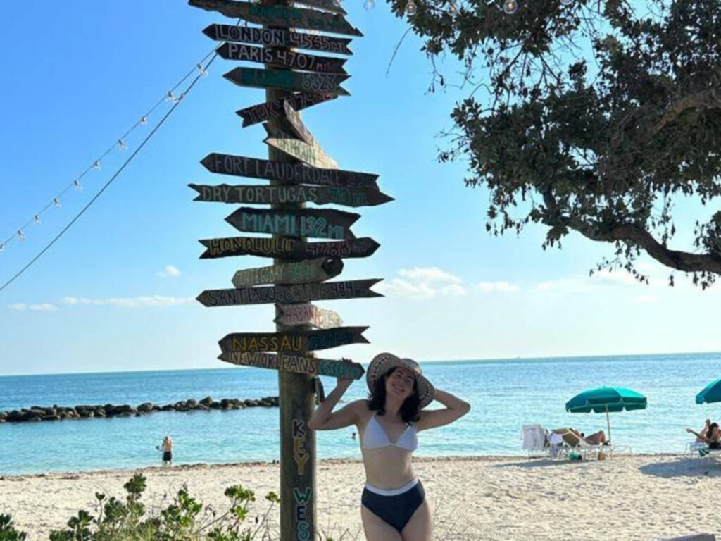 The author Natalie Becerra posing for a photo with the signages at the beach of Fort Zachary Taylor State Park