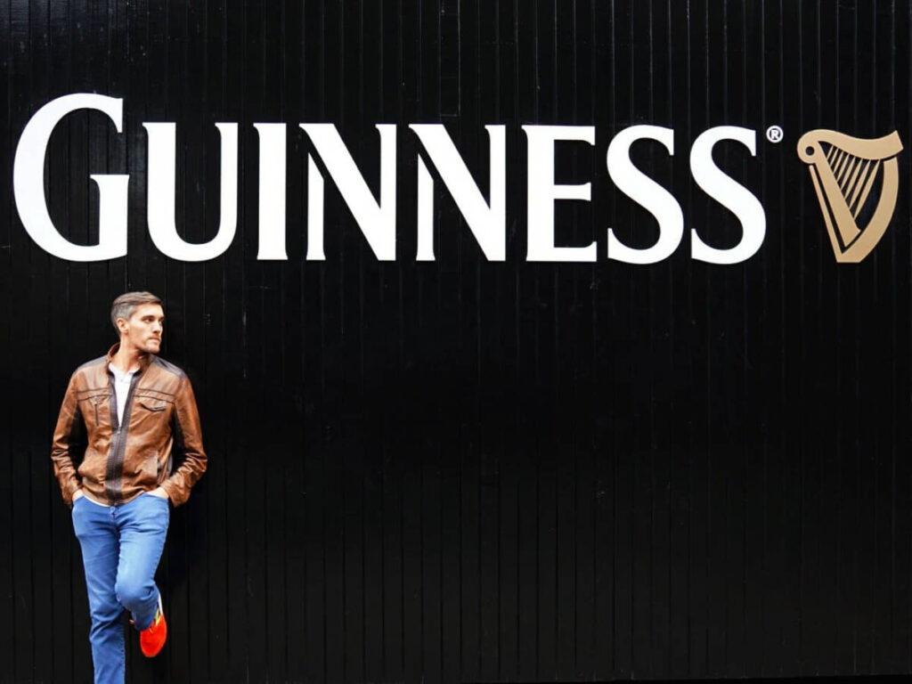 Travel Lemming founder Nate Hake, posing for a photo in front of the Guinness logo against a black wall