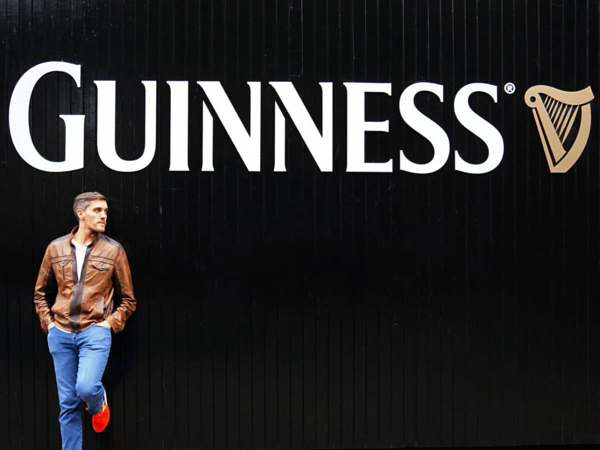 Travel Lemming founder Nate Hake, posing for a photo in front of the Guinness logo against a black wall