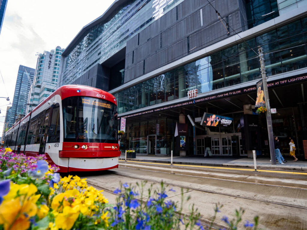 Red train passing by outside the TIFF Lightbox building on King Street West