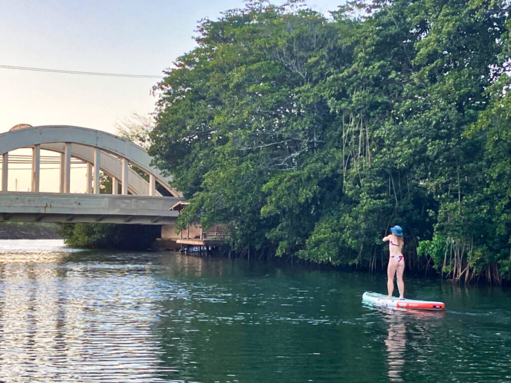 The author Rebecca Parsons paddle boarding in front of the Haleiwa bridge on Anahula River