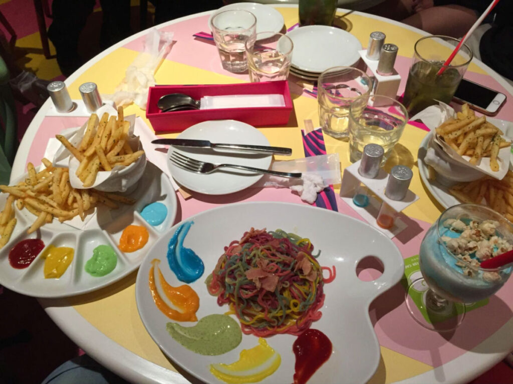 View of a table at a themed restaurant featuring paint palette of rainbow-colored pasta and other colorful meals