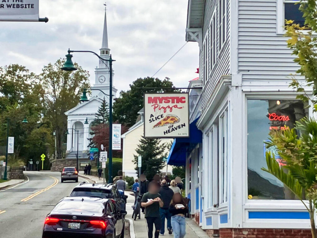 View of the people eating and standing outside the Mystic Pizza seen from across the road