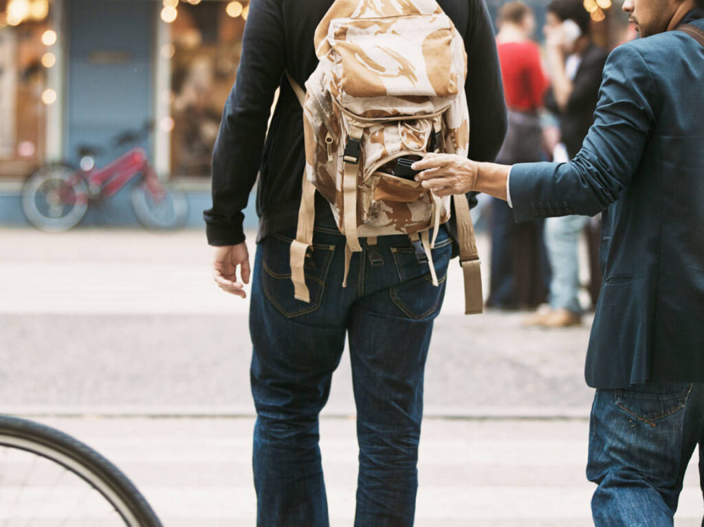 A man stealing the wallet from another man's backpack while walking
