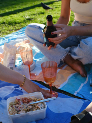 A hand pouring a drink on the glasses at a picnic in the park