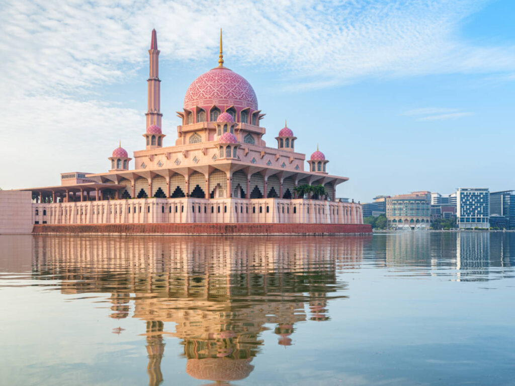 The skyline behind the blushing pink dome of the Putra Mosque reflecting on the water