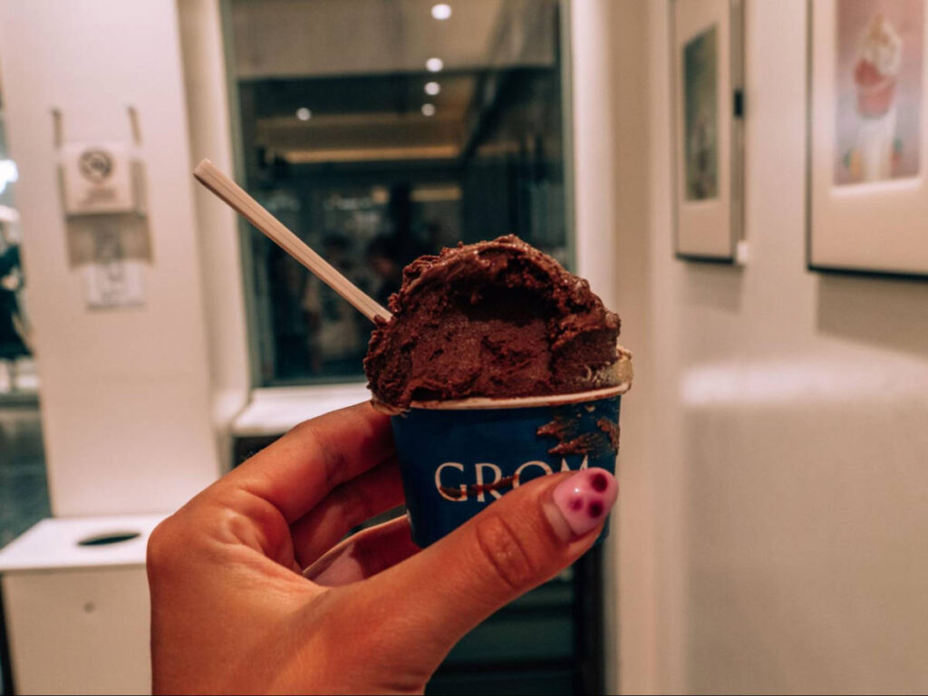 A hand holding a cup of pistachio and dark chocolate ice cream