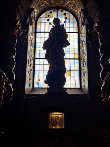 The silhouette of the statue of Mary and the stained glass window inside the church