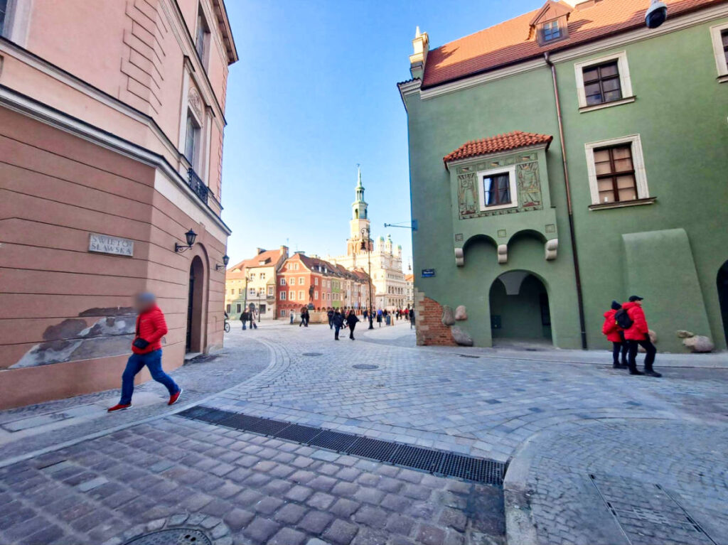 A man walking down on a cobblestone street with pastel-colored buildings around