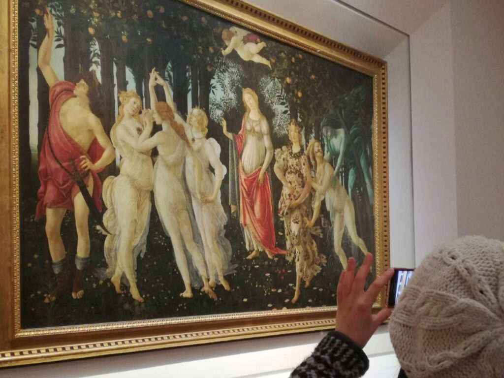 A woman taking a photo of the Primavera by Botticelli inside the Uffizi Gallery