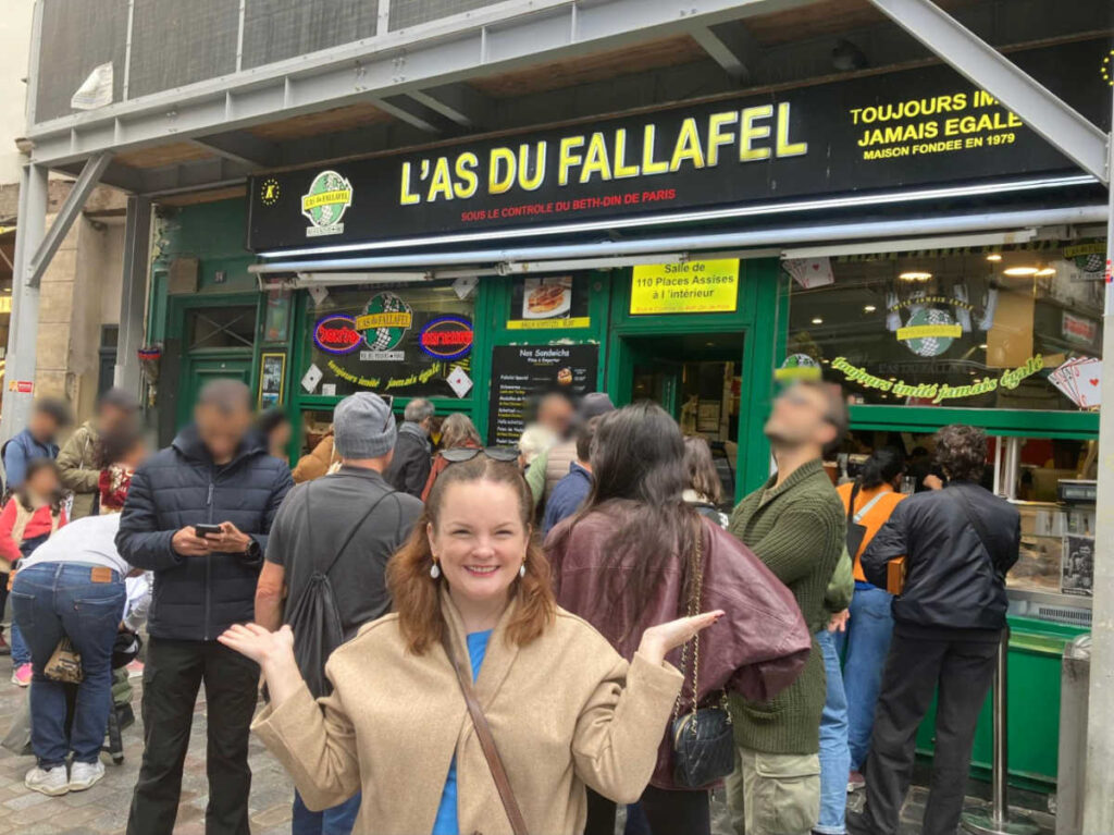 The author Rachel Kapelke-Dale, smiling for a photo on a crowded outside the L’As du Fallafel