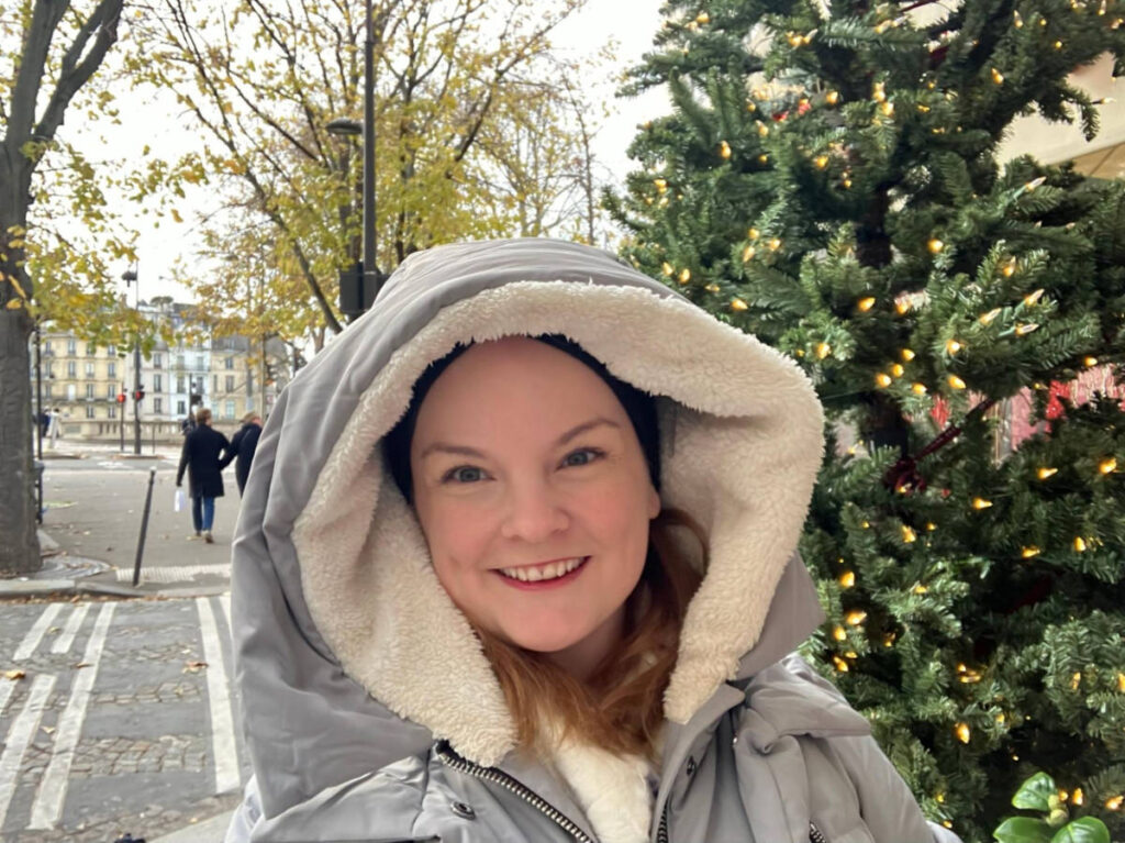 The author Rachel Kapelke-Dale, smiling in front of the decorated Christmas trees