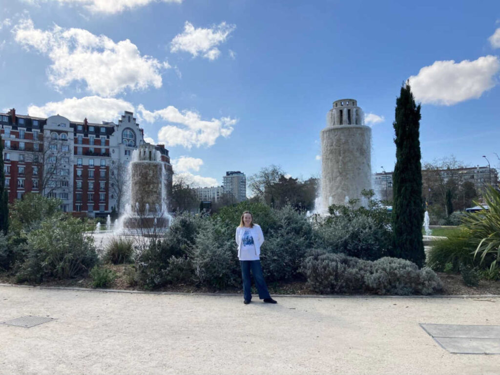 The author, Rachel Kapelke-Dale, standing in front of the fountain at the Place de la Porte de Saint Cloud