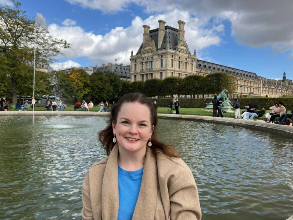 The author Rachel Kapelke-Dale, smiling for a photo in the Tuileries Gardens