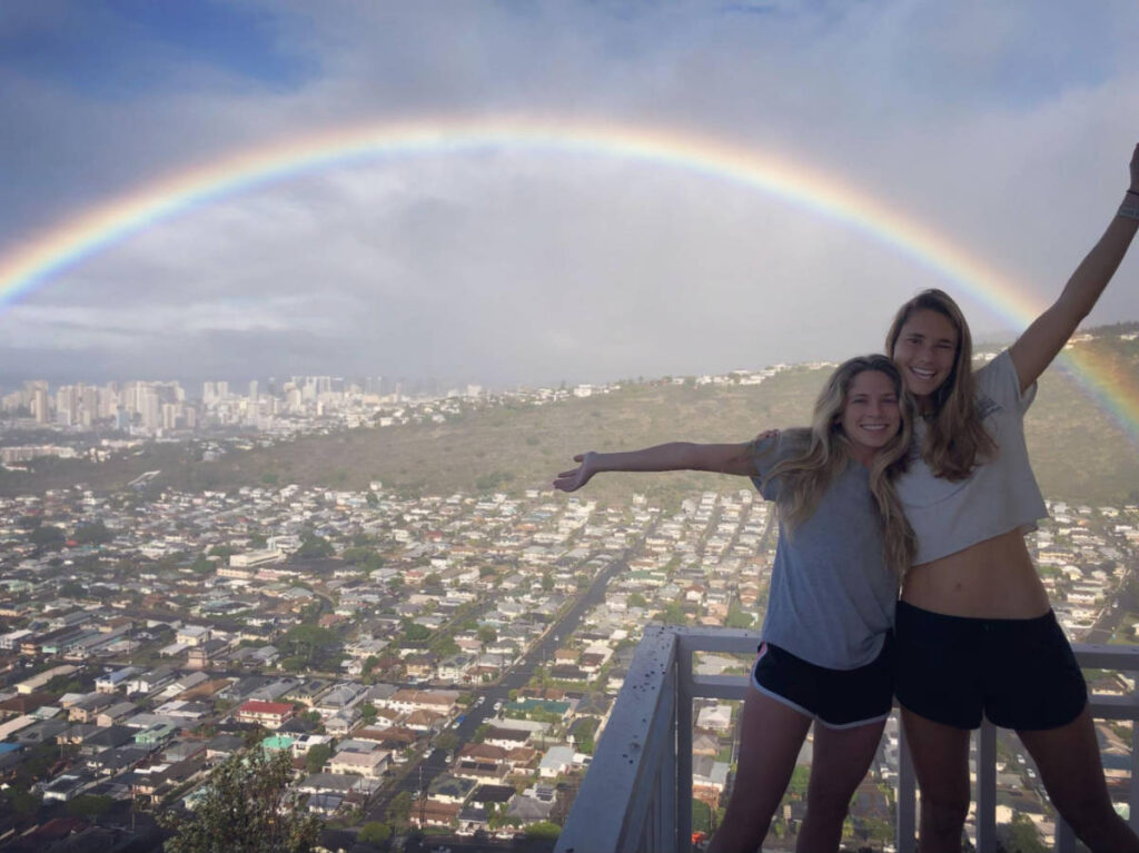 The author Rebecca Parsons and a child posing for a photo with the rainbow over the skyline and mountain of Hawaii