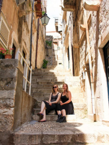 Author Taylor and her friend sitting on steps of an old stone building in Dubrovnik.