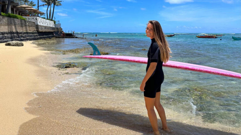 The author Rebecca Parsons holding a surfboard along the shoreline of Oahu’s Gold Coast