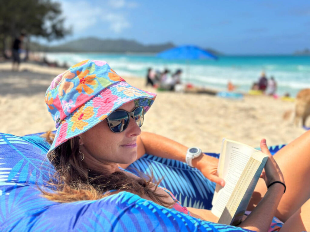 The author Rebecca Parsons reading a book in front of the beach