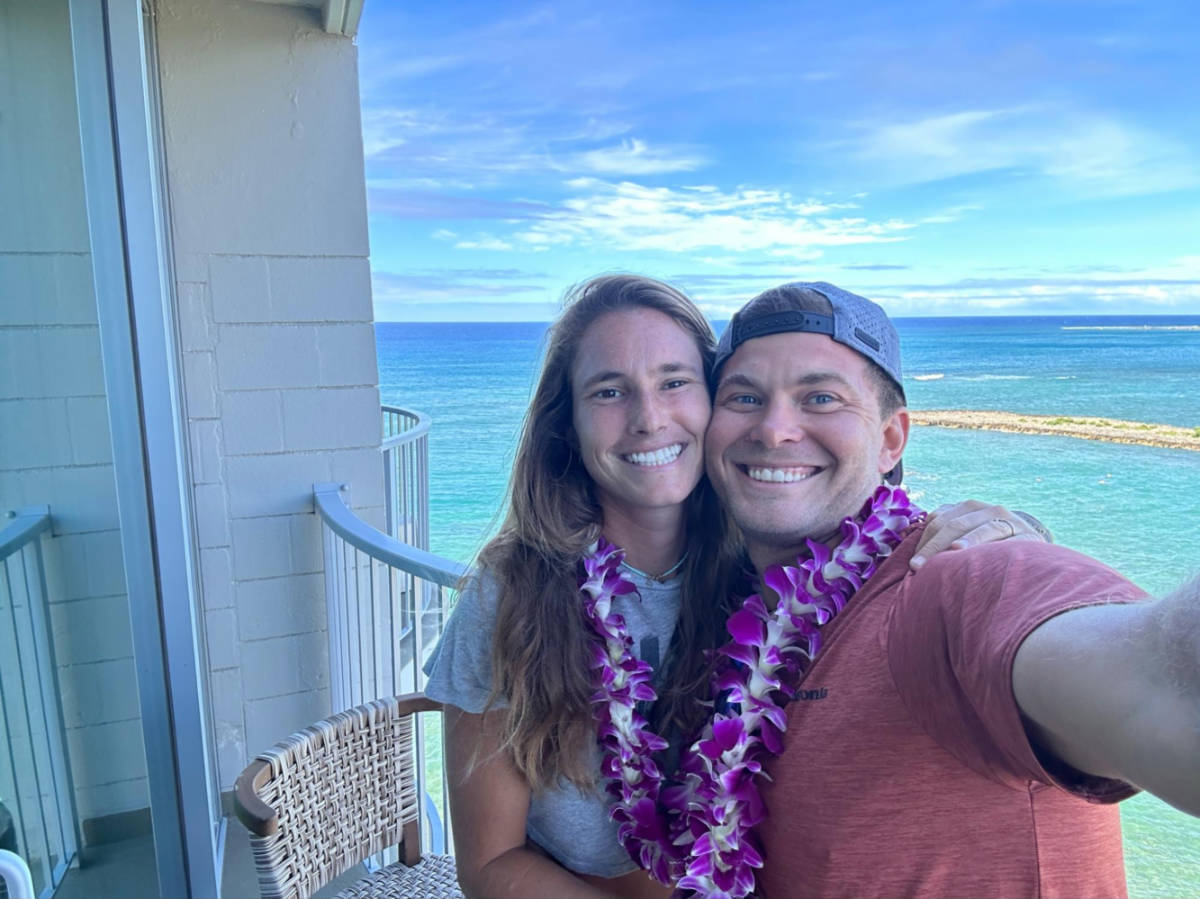 A couple smiling for a photo at the lanai of their hotel room at The Ritz-Carlton O'ahu