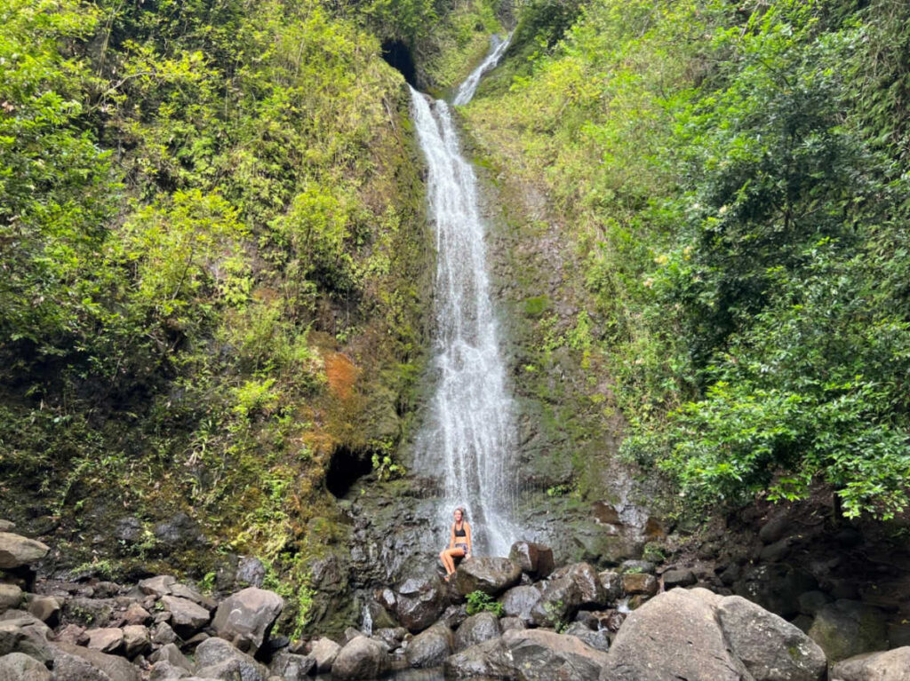 The author Rebecca Parsons sitting on the rock below the Lulumahu Falls