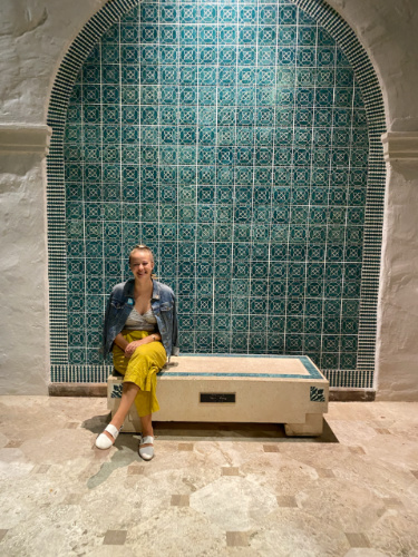The author Rebecca Parsons sitting in front of the tiled walled in Honolulu Museum of Art