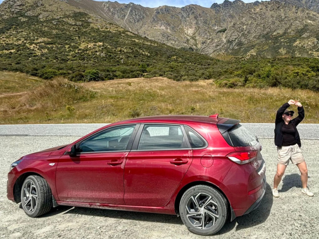 A red rental car parked on a street in Queenstown